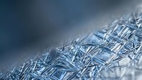 Macro shot of frost crystals forming intricate geometric patterns on frozen surface, suitable for winter backgrounds and seasonal design projects.