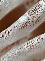 Delicate white lace fabric with floral pattern shown in macro detail against soft brown background, creating elegant texture and depth for wedding and fashion designs.