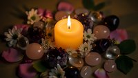 Burning orange candle surrounded by healing crystals, dried flowers and gemstones creating mystical spiritual atmosphere for meditation and wellness rituals.