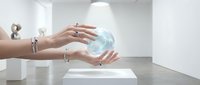 Female hands with silver rings holding glowing holographic sphere in modern white interior space for futuristic technology and innovation concepts.