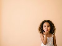 Young girl with curly dark hair and medium skin tone blowing a kiss against a warm beige background, expressing affection and joy for greeting cards, family portraits, and children's content.