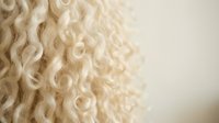 Soft cream-colored curly wool texture with natural fibers creating organic patterns. Close-up macro photography showing detailed spiral curls and loops.