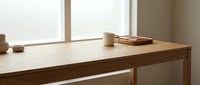 Minimalist wooden desk with coffee cup and notebooks by bright window creating warm natural lighting for modern home office workspace interior design.