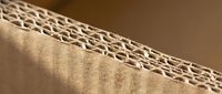 Corrugated cardboard edge showing detailed fluted structure and brown kraft paper layers for packaging and shipping applications.