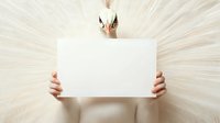 Young Asian woman holding blank white card against beige tulle background, minimalist artistic portrait with soft ethereal lighting and delicate composition.