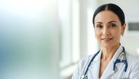 Professional female doctor with stethoscope smiling confidently in modern medical office setting for healthcare and wellness concepts.