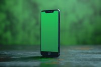 Modern smartphone standing upright on wet surface against blurred green nature background, showcasing minimalist technology composition for advertising and marketing use.