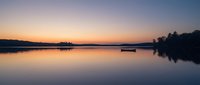 Serene lake at sunrise with moored boats and forested shoreline reflecting in calm water during golden hour.