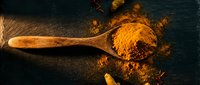 Golden turmeric powder spilling from wooden spoon on dark slate surface with warm lighting for cooking and spice photography.