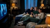 Family of three relaxing on couch watching television together in cozy living room at night with warm lighting and popcorn for entertainment and bonding.
