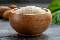Raw white jasmine rice in round bamboo bowl on dark stone background with green leaves and brown eggs, macro food photography for cooking blogs.