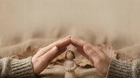Young woman hands in beige sweater protecting wooden figurine symbolizing care, safety and protection concepts for family insurance and security.