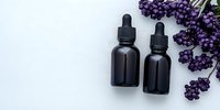 Black glass dropper bottles with fresh lavender sprigs on white background, minimal spa composition for aromatherapy and essential oils packaging design.