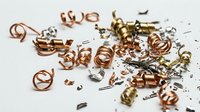 Scattered copper wire coils and brass components with metal shavings on white surface, suitable for electronics, recycling, industrial, and manufacturing concepts.