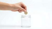 Hand dropping coin into clear glass jar on white background, savings and financial investment concept for banking and money management.