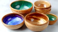 Handcrafted wooden bowls with vibrant glazed interiors in blue, green, and amber colors arranged on white surface, showcasing artisanal craftsmanship and natural materials.