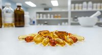 Colorful vitamin capsules and pills scattered on white laboratory counter with blurred pharmacy background for health and wellness supplement concepts.