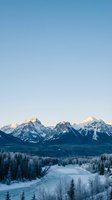 Snowy mountain range with frozen lake and evergreen forest at sunrise, showcasing winter landscape scenery for travel and nature design projects.