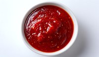 Fresh homemade tomato sauce in white ceramic bowl on light background, top view close up of thick red marinara sauce with visible texture and spices.