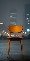 Wooden chair illuminated by warm street lights against blurred urban nightscape with bokeh lights and skyscrapers, creating moody atmospheric composition.