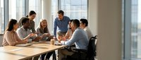 Diverse business team collaborating in modern conference room with natural lighting and city view windows for corporate meetings and strategy sessions.