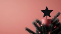 Minimalist Christmas composition with black star tree topper on pink background, fir branches and glowing lights creating festive holiday atmosphere.