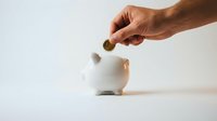 Hand dropping coin into white piggy bank on clean background for savings and financial planning concepts.