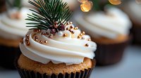 Festive winter cupcake with swirled white frosting topped with pine sprigs, golden pearls and bronze sprinkles against blurred holiday lights background.