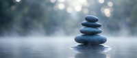 Zen stone stack balanced on calm water surface with soft bokeh lights creating peaceful meditation atmosphere for wellness and mindfulness concepts.