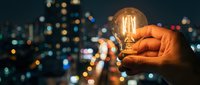 Hand holding glowing vintage Edison bulb against blurred city lights at night, symbolizing innovation, creativity and bright ideas for business concepts.
