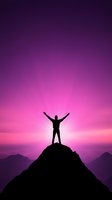 Silhouette of person with raised arms standing on mountain peak against dramatic purple and pink sunset sky, expressing freedom and achievement.