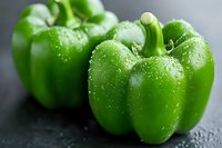 Fresh green bell peppers with water droplets on dark surface for healthy cooking and nutrition concepts.