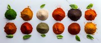 Colorful spice powder collection with fresh basil leaves arranged in rows on white background, featuring vibrant turmeric, paprika, cinnamon and exotic seasonings.