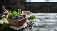Dried lavender flowers in wooden bowl with essential oil bottles and fresh mint on rustic table for aromatherapy and natural wellness treatments.