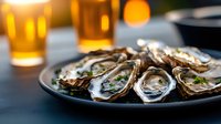 Fresh oysters on black plate garnished with herbs and lemon, served with cold beer in background, creating luxurious seafood dining atmosphere.