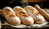Fresh baked crusty French baguettes with golden brown crust on rustic wooden surface dusted with flour, steam rising in warm bakery lighting.