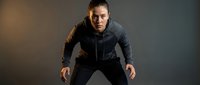 Determined athletic woman in gray hoodie and black leggings in a powerful stance, focused expression, dark studio background, fitness motivation.
