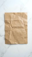 Crumpled brown kraft paper sheet with wrinkled texture on marble surface for packaging design and eco-friendly branding projects.