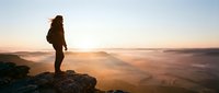 Hiker with backpack standing on rocky mountain peak at sunrise overlooking misty valley landscape, adventure and outdoor exploration concept.