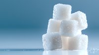 White sugar cubes stacked in creative composition on blue gradient background with soft focus and water droplets, demonstrating sweetness and purity in food photography.