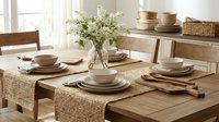 Rustic wooden dining table set with natural woven placemats, ceramic dinnerware and fresh white flowers in modern farmhouse kitchen interior.