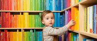 Curious toddler girl reaching for colorful books on library shelves, early childhood education and learning development concept for educational materials.