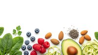Healthy superfood ingredients including avocado, berries, nuts and leafy greens arranged on white background for clean eating and nutrition concepts.