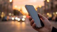 Hand holding smartphone with blank screen against blurred city lights at sunset, perfect for mobile app mockups and digital communication concepts.