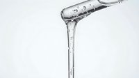 Clear liquid pouring from measuring cup with water droplets and splashes against white background for beverage, cooking, and scientific content.