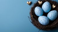 Spotted blue Easter eggs in dark twig nest with golden heart decorations on blue background. Minimal spring holiday composition for seasonal cards and designs.