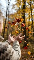 Person tossing autumn leaves in the air with hands wearing a cozy sweater in a forest with golden foliage and trees.