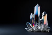 Clear quartz crystal cluster with iridescent rainbow colors against dark background, showing natural mineral formation and light refraction properties.