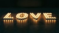 Word LOVE spelled out with glowing tealight candles on dark floor, warm romantic atmosphere for Valentine's Day or wedding concepts.
