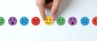 Hand selecting yellow smiley face among colorful emotion balls representing customer satisfaction, feedback rating, and service quality assessment for business evaluation.